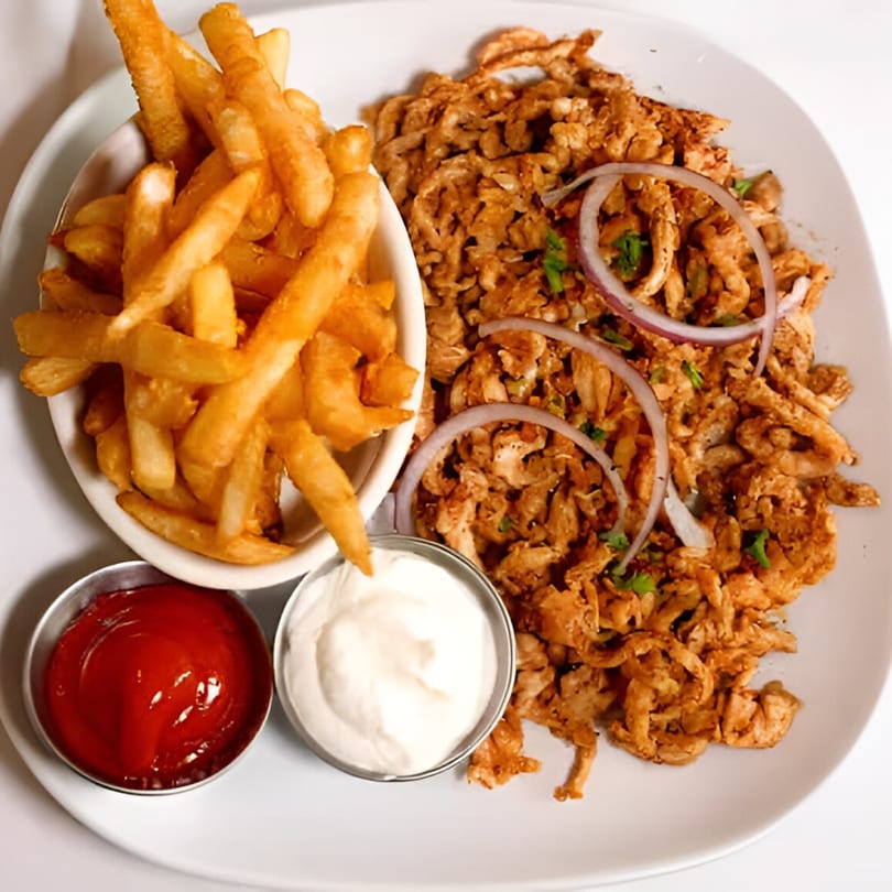 Mediterranean chicken shawarma with red onion, parsley, a side of french fries, ketchup, and garlic sauce.