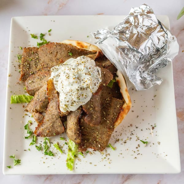 Mediterranean gyro meat with tzatziki sauce and herbs on pita bread, with foil-wrapped food.
