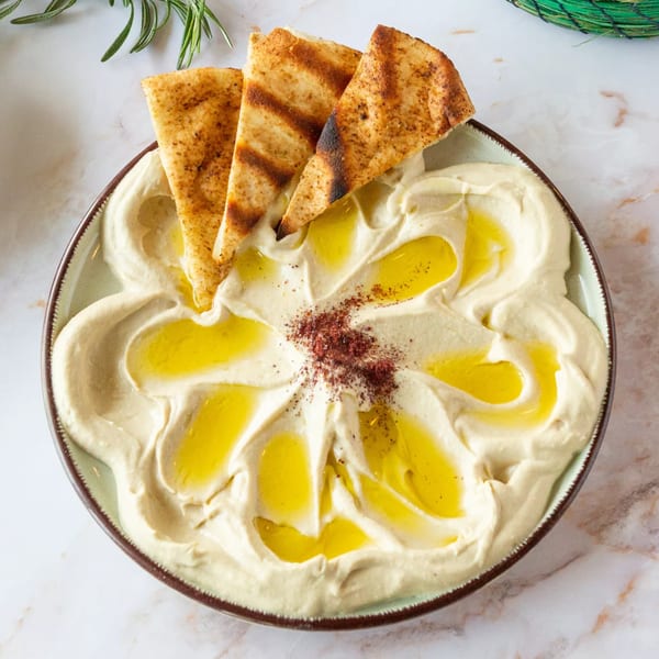 Creamy hummus with olive oil, sumac, and grilled pita bread on a marble surface.