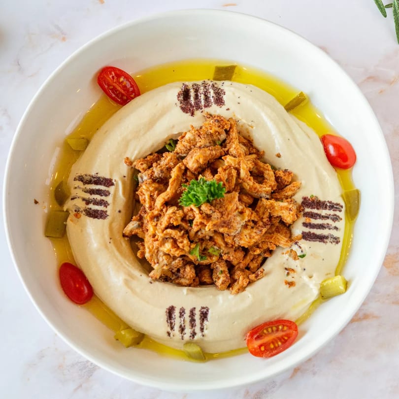 Creamy hummus topped with seasoned chicken shawarma, olive oil, cherry tomatoes, and pickles.
