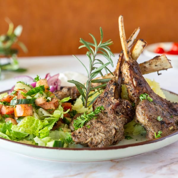 Grilled lamb chops with fresh Mediterranean salad, garnished with rosemary and parsley.