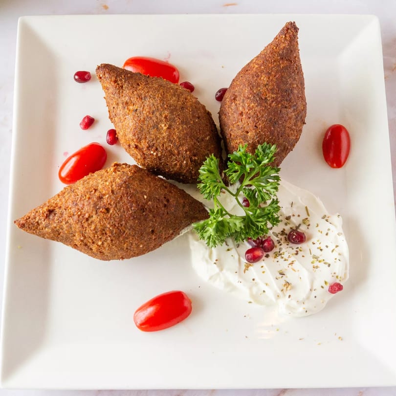 Three kibbeh, a Mediterranean dish, with cherry tomatoes, pomegranate seeds, and a dollop of yogurt.